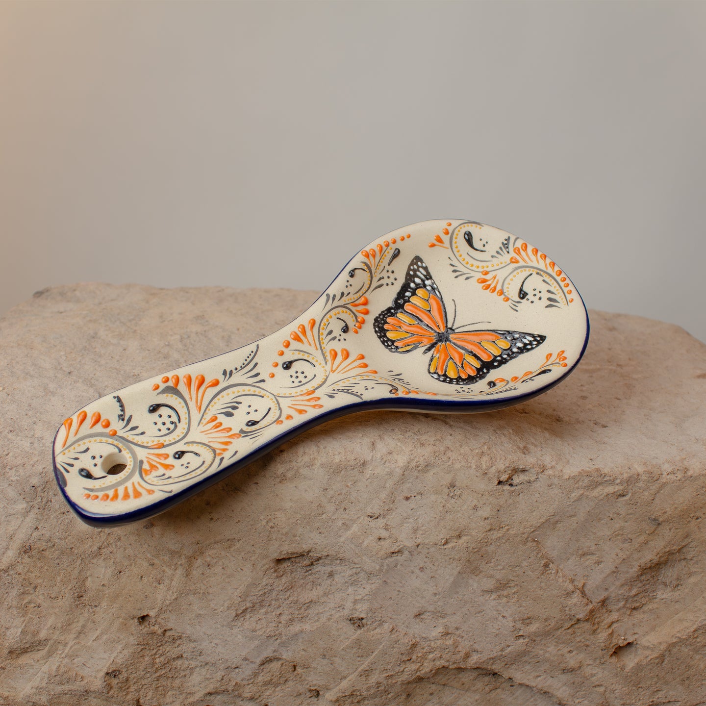 Stoneware spoon rest with butterfly design on a stone surface