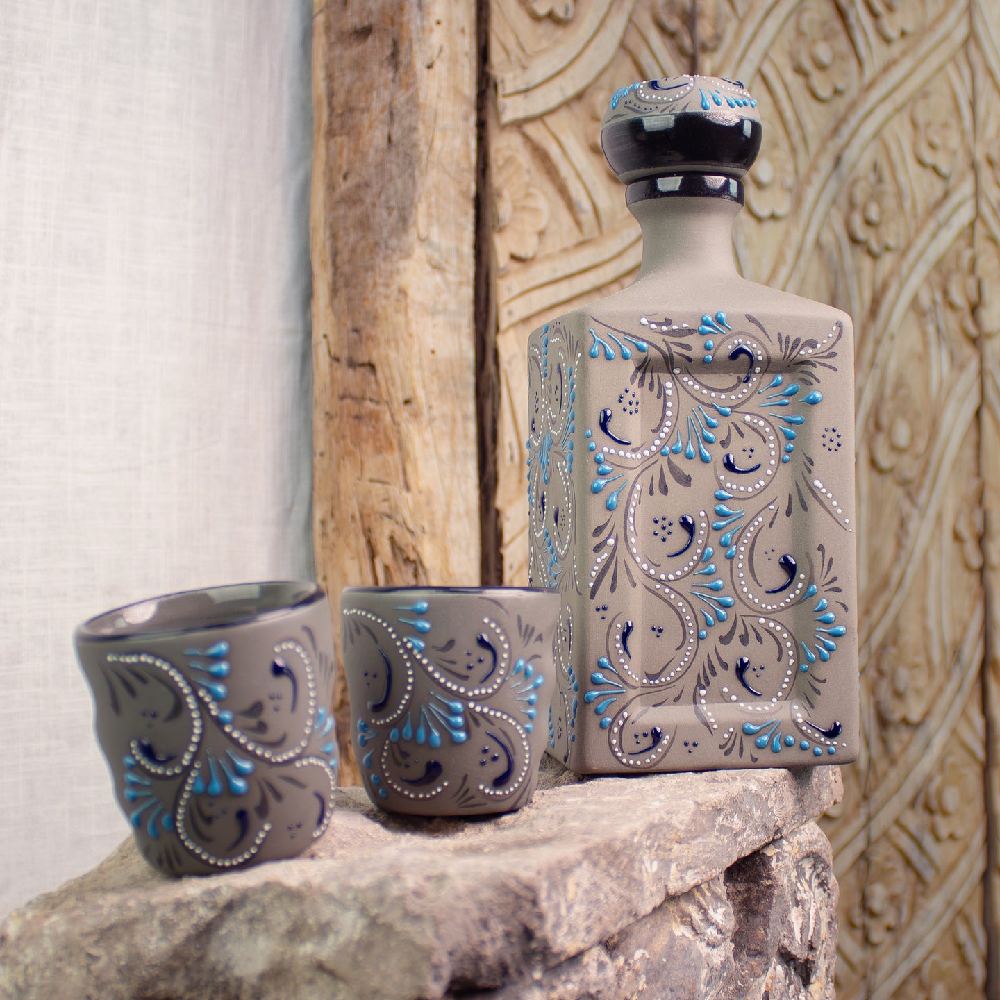 Ceramic decanter and two cups with intricate blue patterns on stone surface.