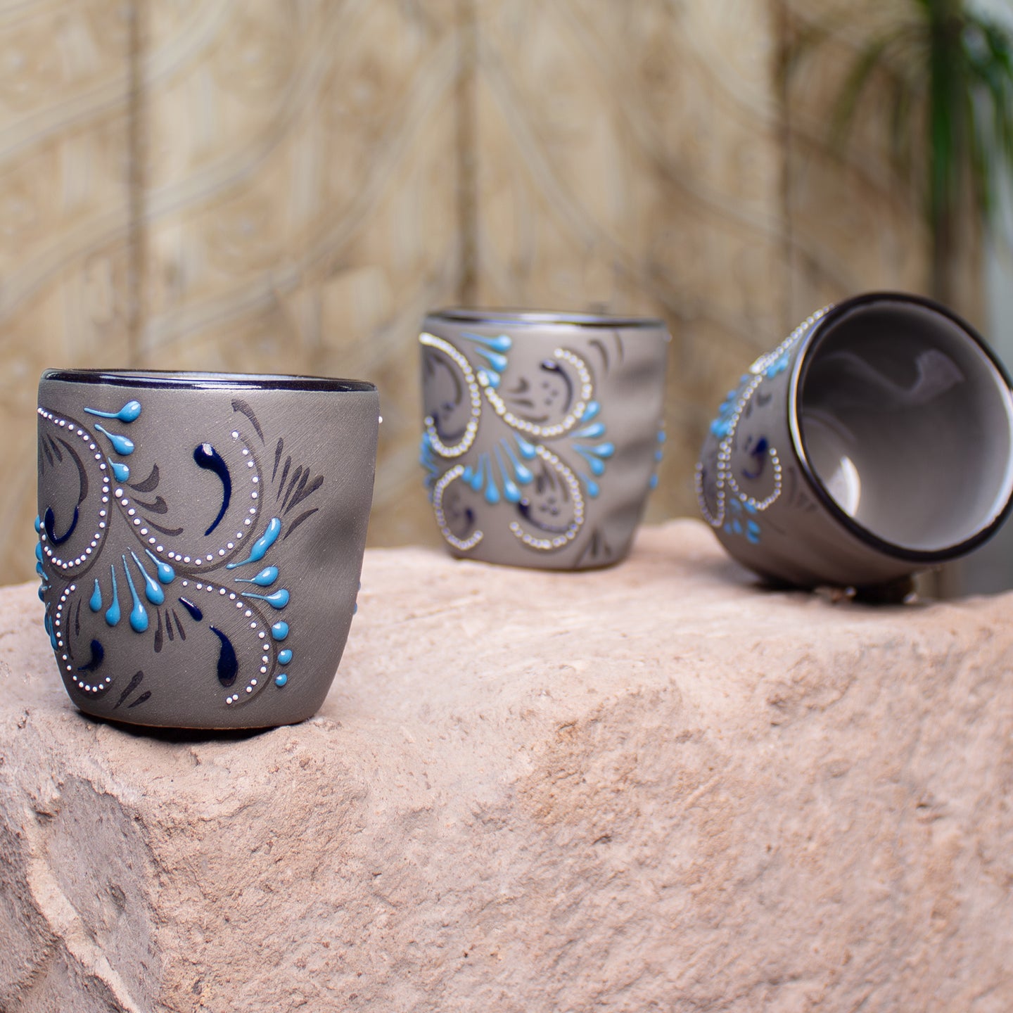 Three gray ceramic cups with blue and white decorative swirl patterns, displayed on a stone conter top with blurred background.