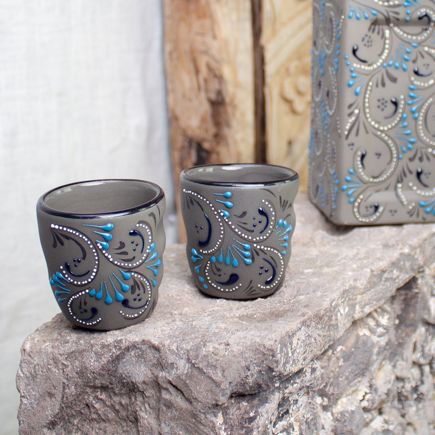 Two gray ceramic candle holders with blue and white hand-painted floral patterns sit on a stone surface.