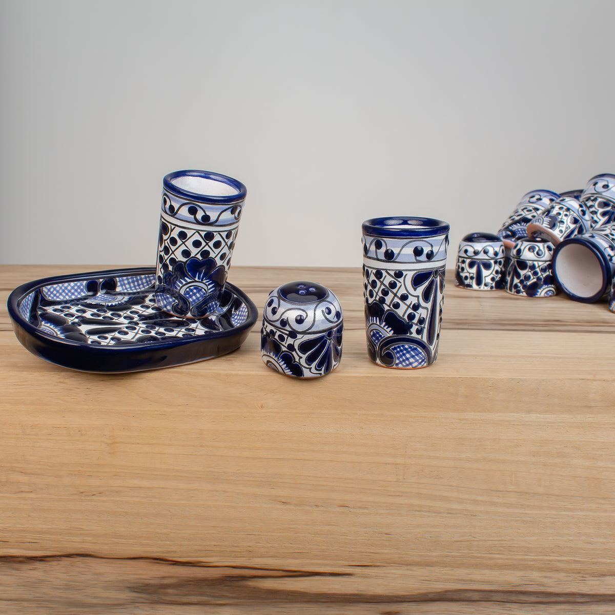 Four-piece ceramic tequila serving set in traditional blue and white Talavera. The four piece set includes a shallow oval tray, two 4 ounce shot glasses, and a salt shaker, all decorated with the same vibrant hand-painted pattern.