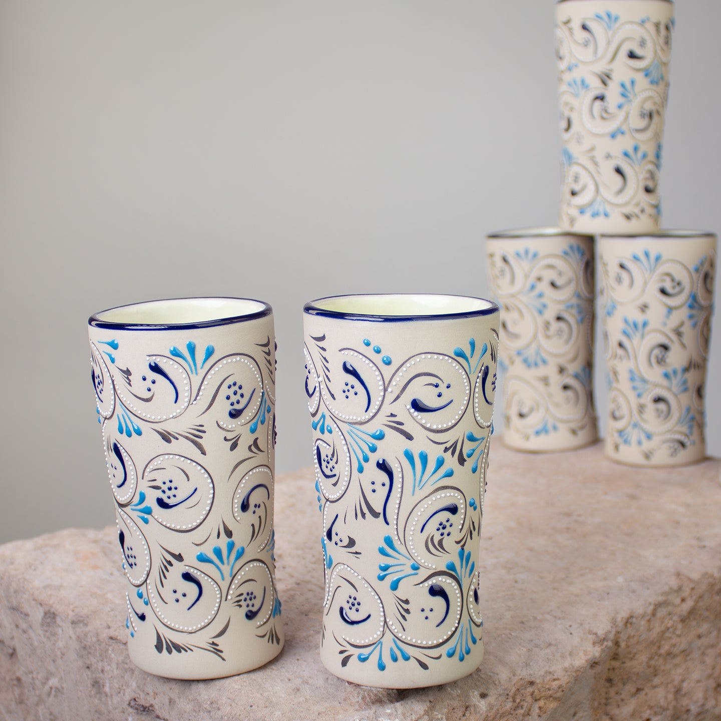 Two tall ceramic tumblers with blue and black floral scroll patterns on a cream background, displayed on a stone surface.