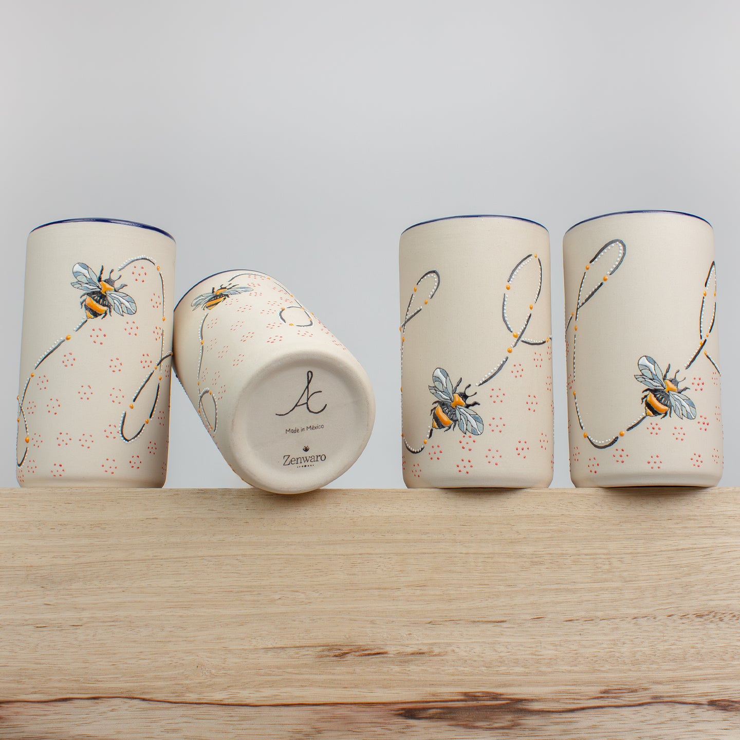 Stoneware tumblers with bee designs on a wooden counter.