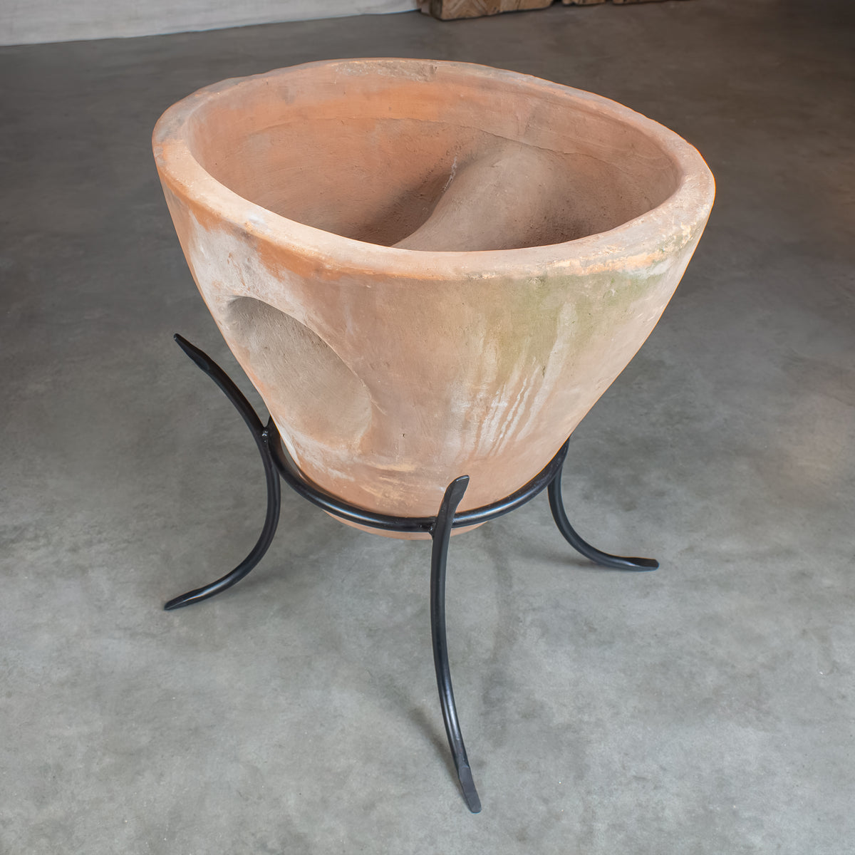 A large terracotta planter pot with a double-compartment design, displayed on a black metal stand on a patio floor.