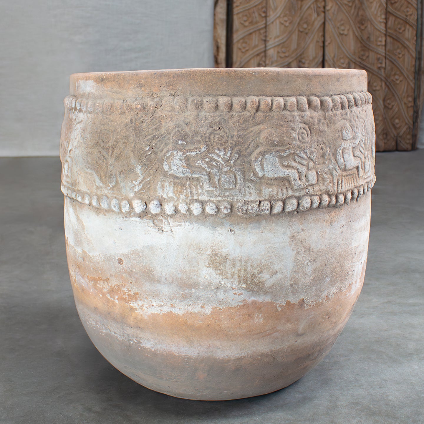 Decorative terracotta pot with intricate designs on concrete surface.