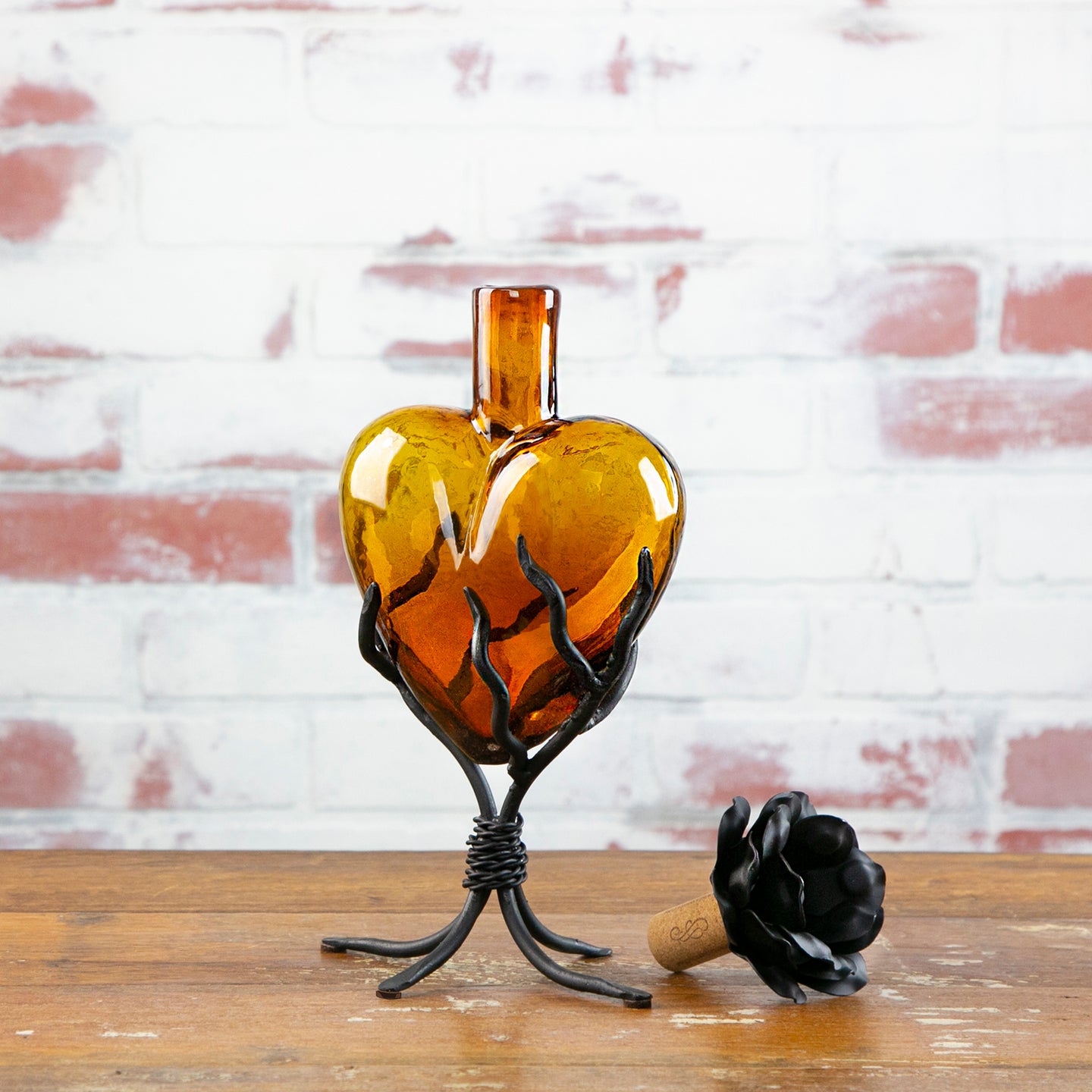 Heart-shaped amber glass bottle with black metal stand against a brick wall.