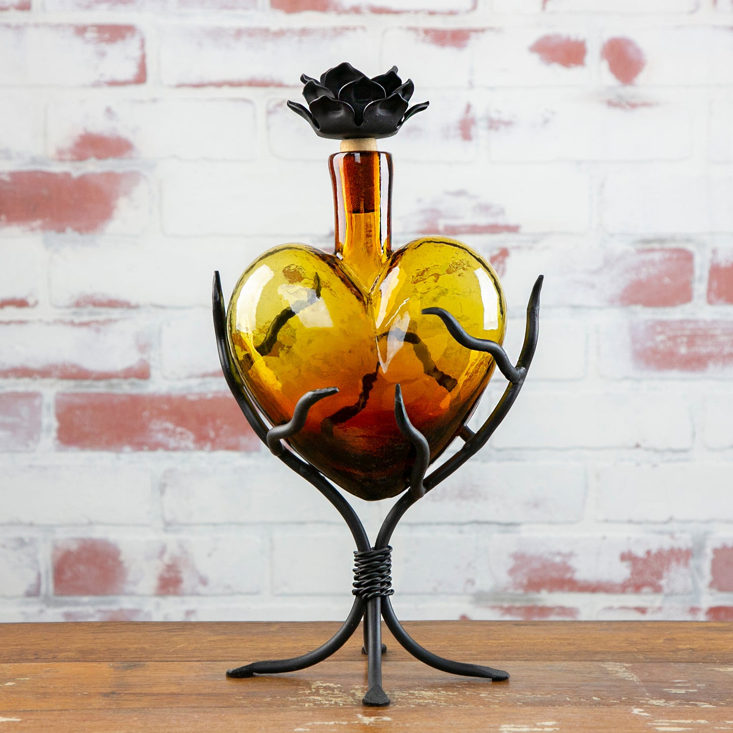Heart-shaped glass vase with metal stand against a brick wall.