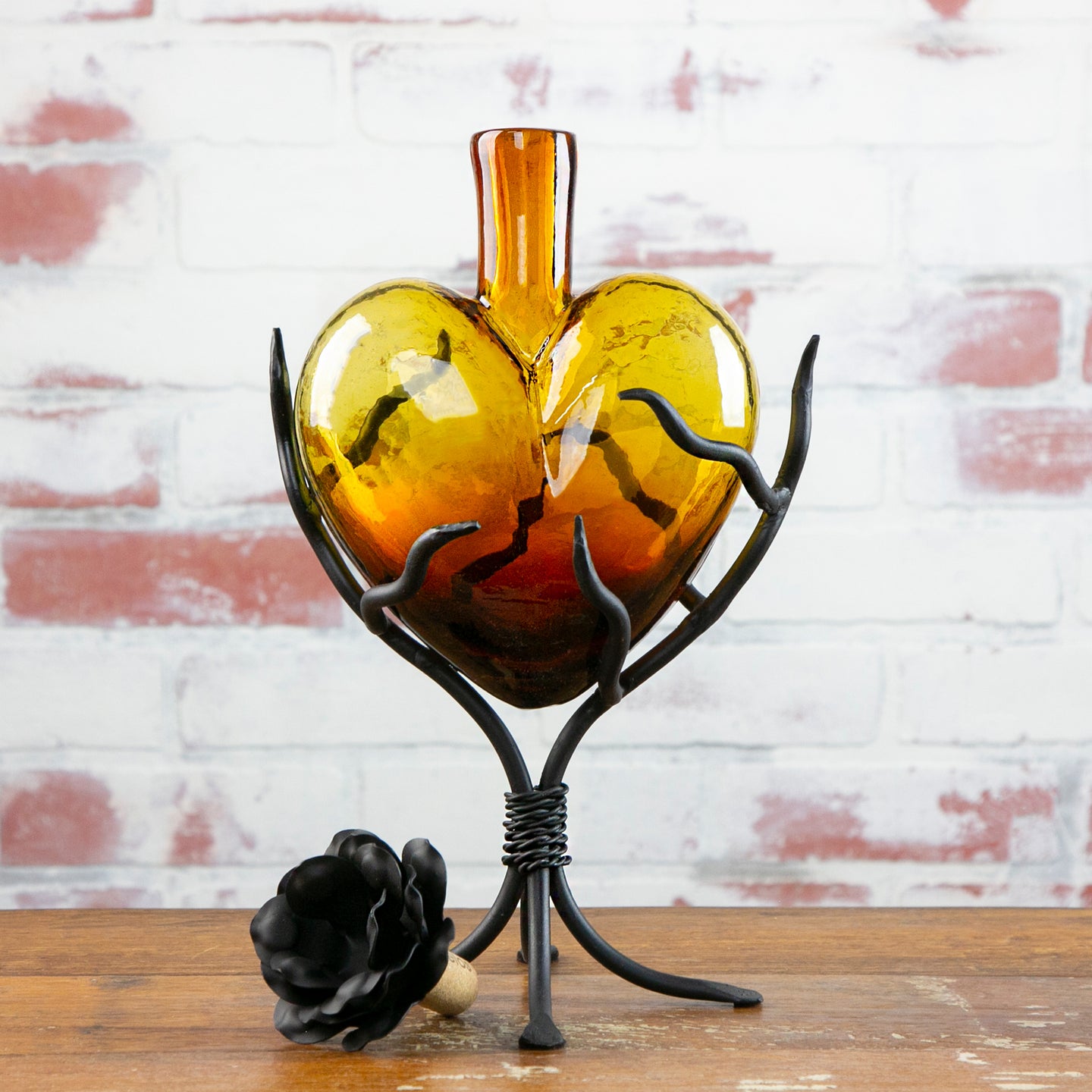 Decorative glass heart decanter with metal stand against a brick wall.