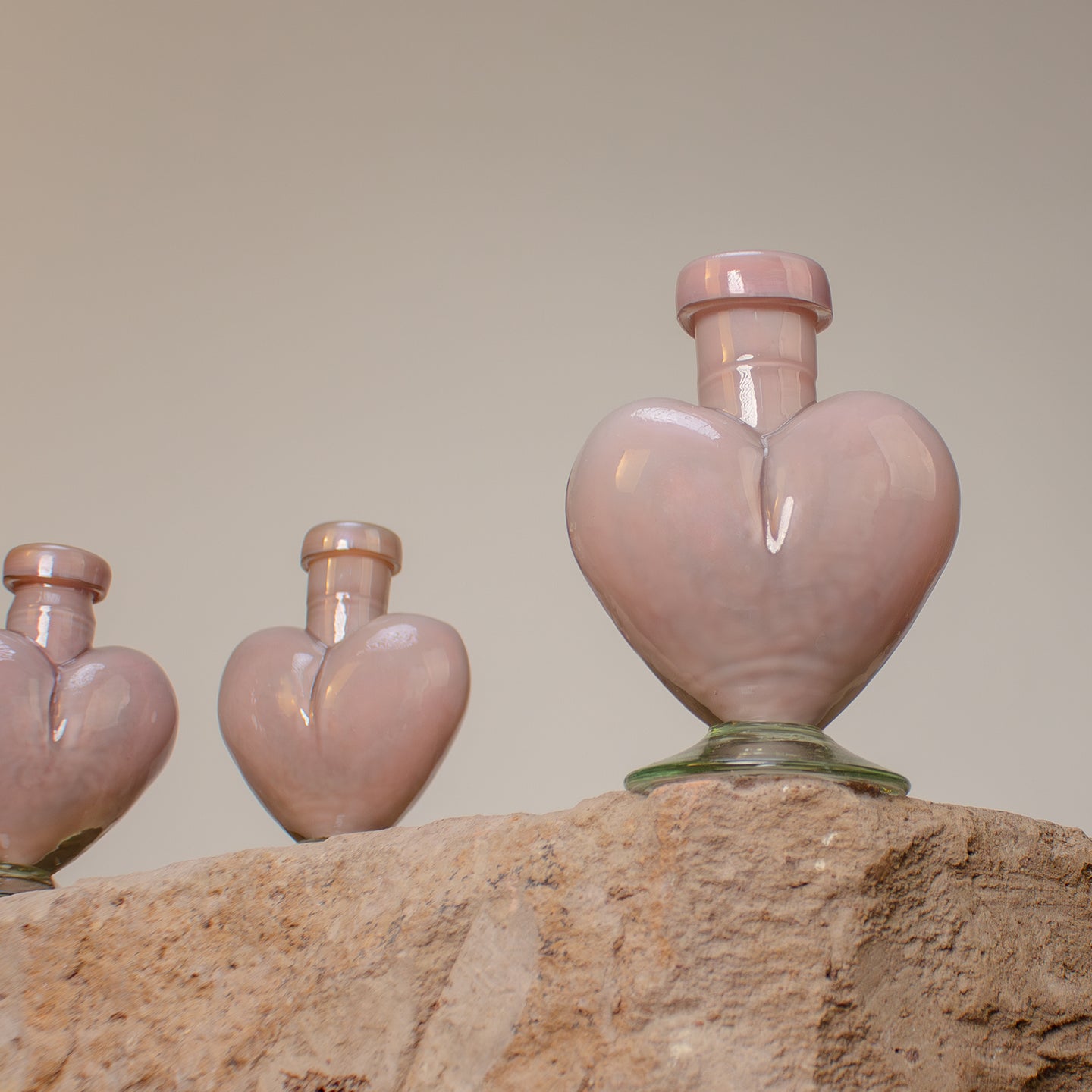 Heart-shaped glass vase resting on stone surface. Small pink glass bottles, hand blown from recycled glass.