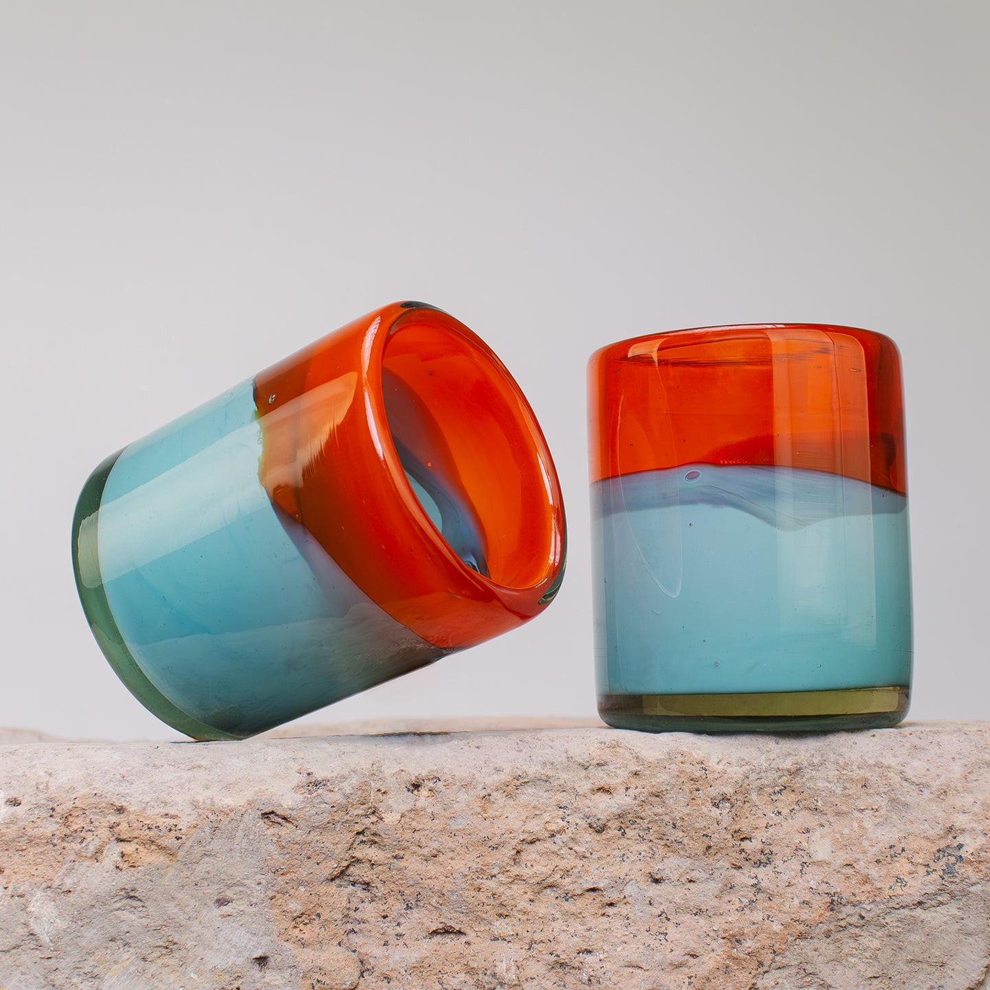 Orange and teal blown glass tumblers on a stone counter.