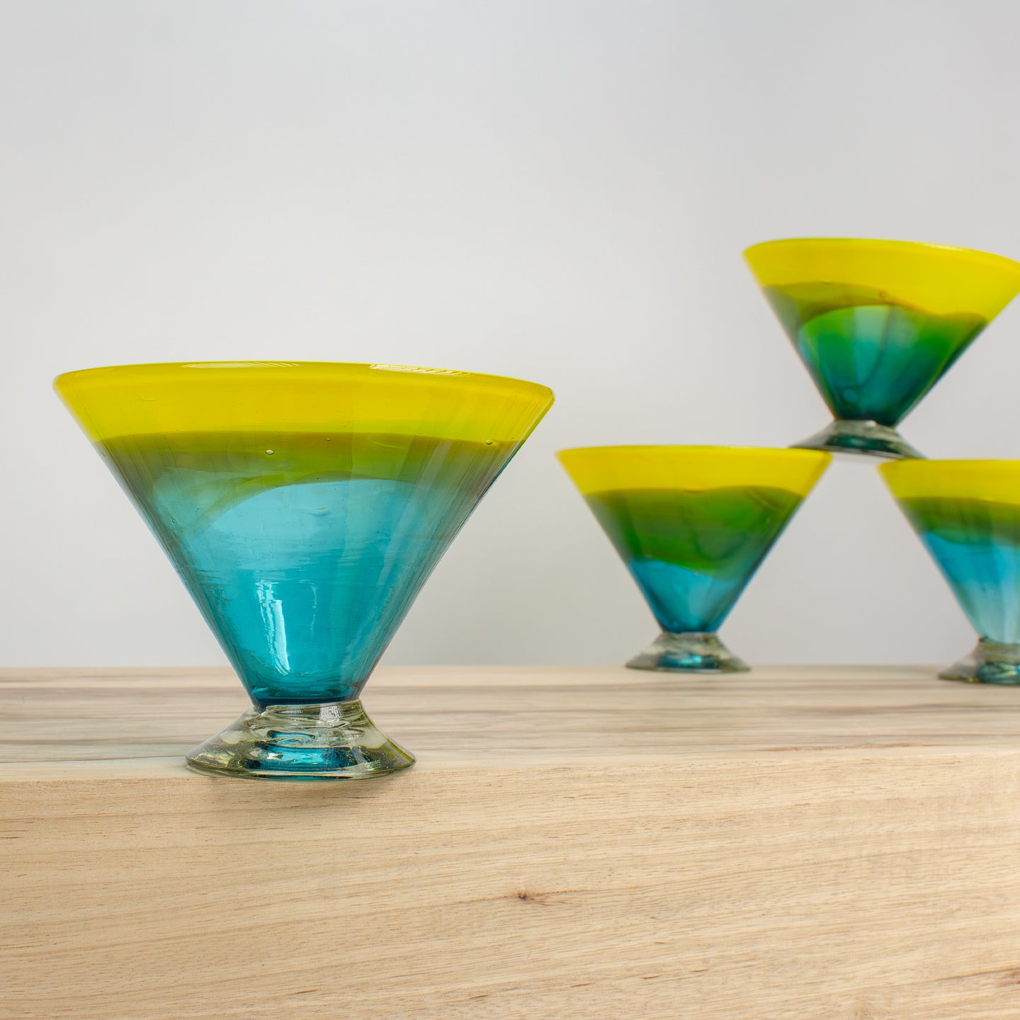 Martini glasses with with cosmic color transition from blue to green to yellow on a wooden counter.